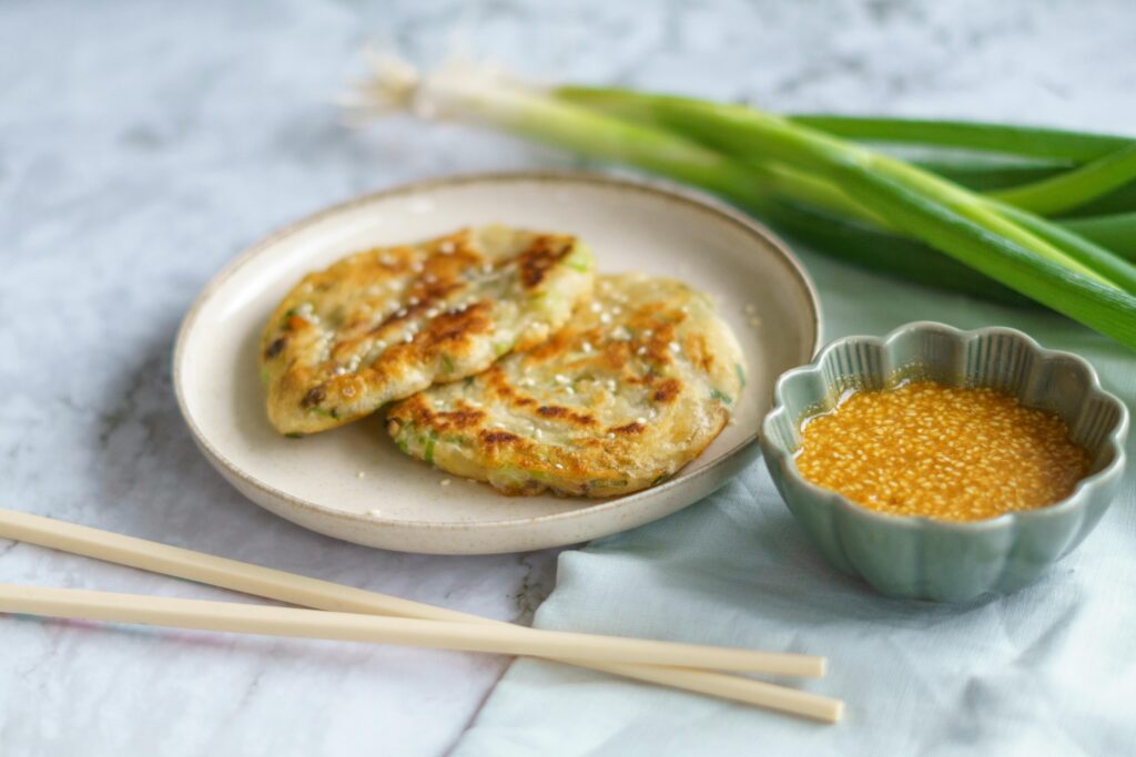 Tasty Korean scallion pancakes served with sesame dipping sauce on a ceramic plate, styled with chopsticks.
